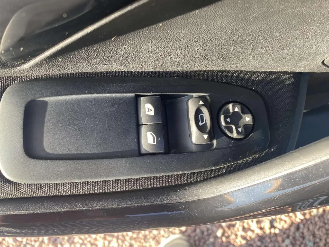 Gros plan sur les commandes électriques des vitres et des rétroviseurs côté conducteur d'une Peugeot 208 noire.