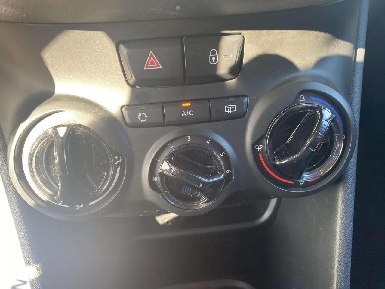 Commandes de climatisation et verrouillage central d'une Peugeot 208 noire, vue rapprochée du tableau de bord.