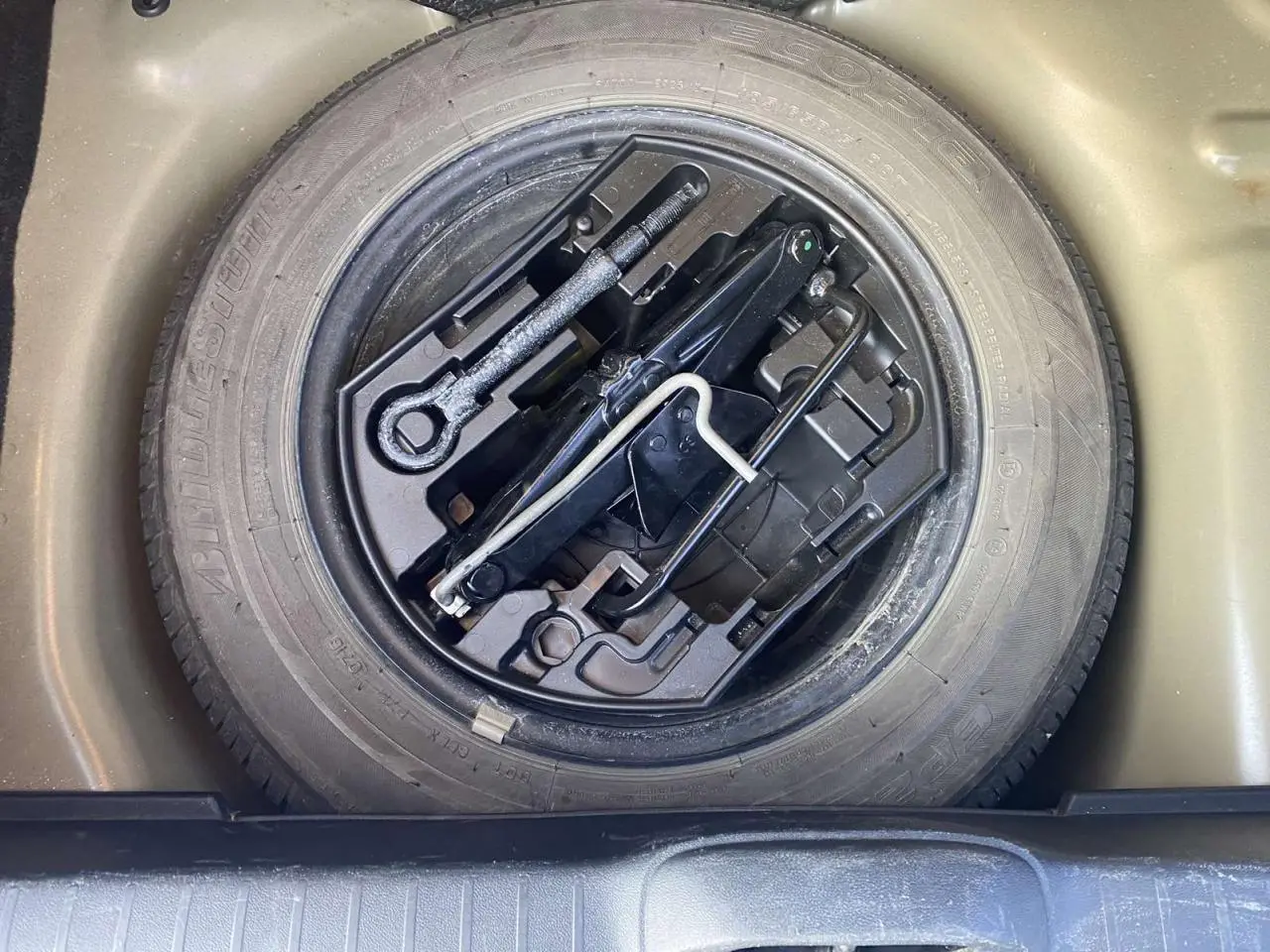 Gros plan sur la roue de secours acier 15 pouces et le cric dans le coffre d'une Peugeot 208 noire 2016.