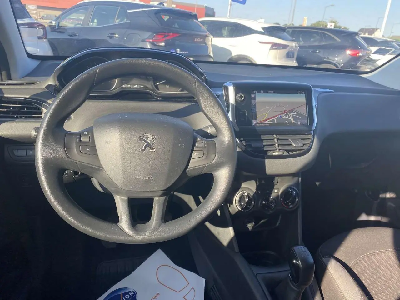 Vue de face de l'intérieur d'une Peugeot 208 noire, volant multifonction et écran tactile GPS au centre du tableau de bord.