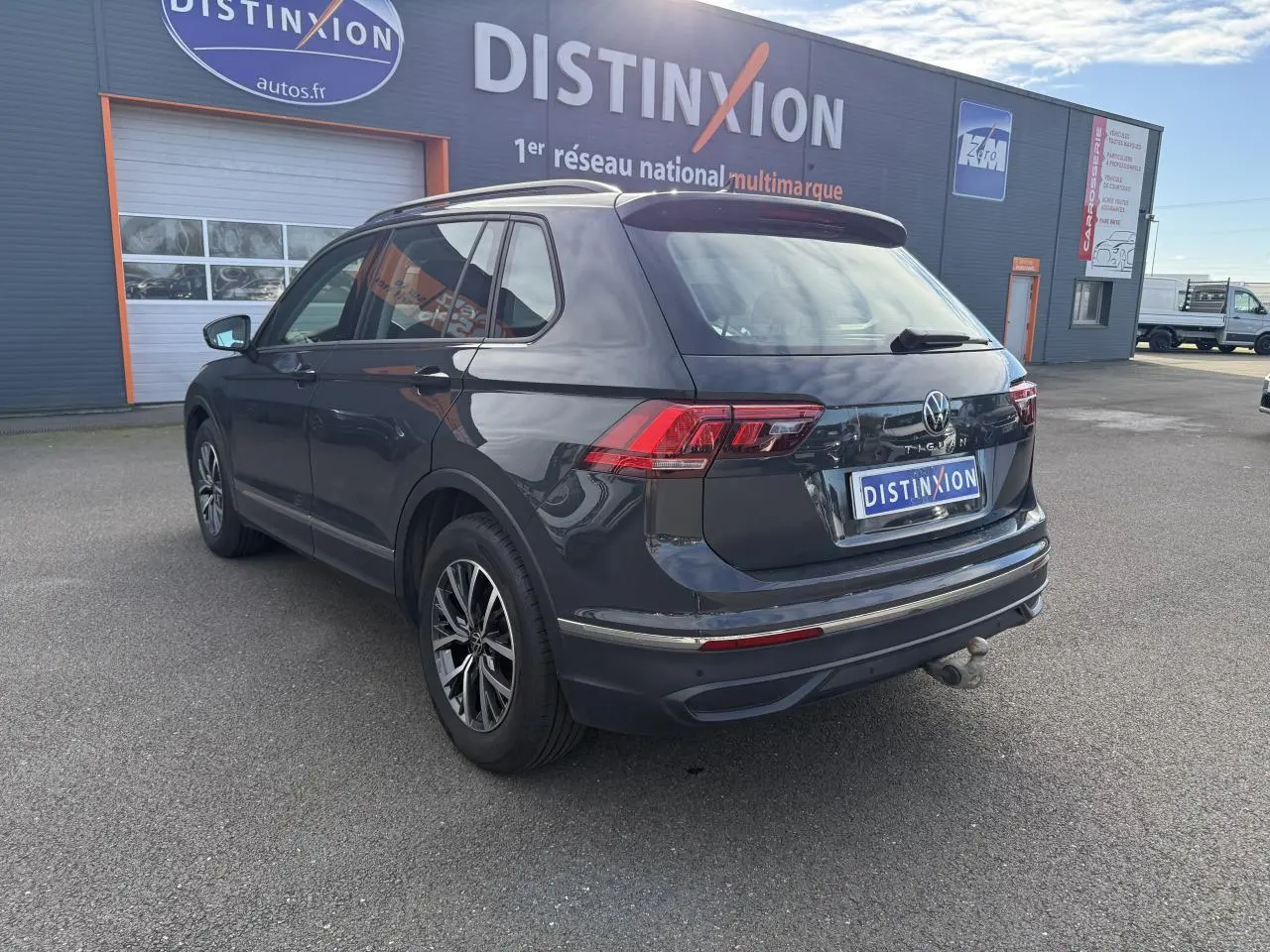 Vue 3/4 arrière droite d'un Volkswagen Tiguan gris Urano avec crochet d'attelage et jantes alliage foncé brillant.
