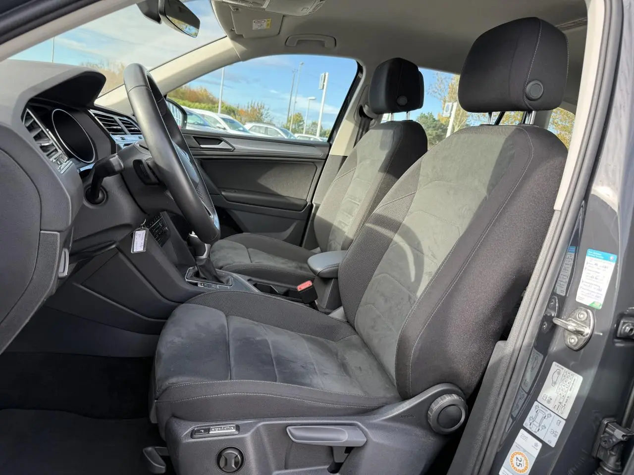 Vue intérieure côté conducteur du Volkswagen Tiguan 2023 gris Urano, sièges ergoActive en tissu et alcantara noirs.