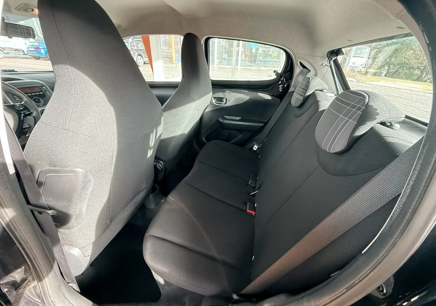 Vue intérieure arrière côté gauche du Peugeot 108 noir montrant les sièges en tissu gris foncé avec appuie-têtes à motifs rayés.