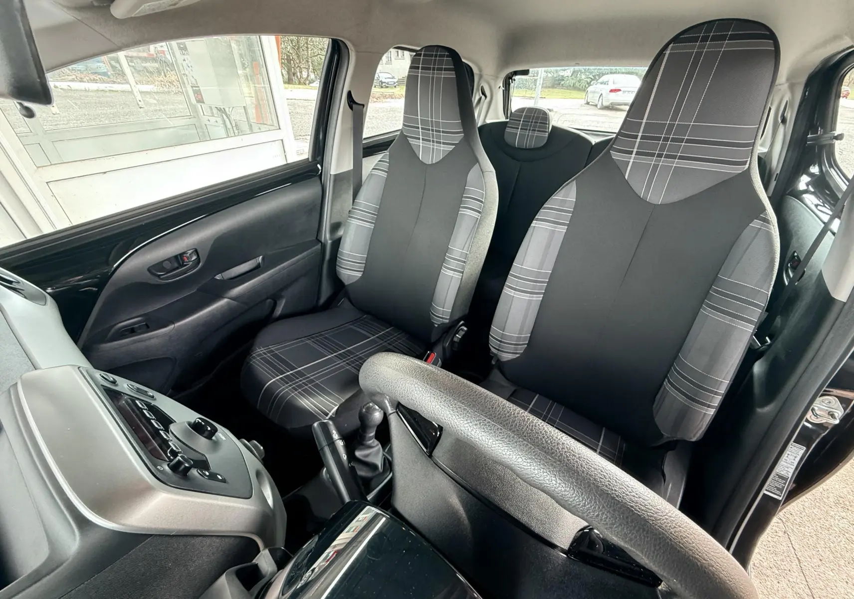 Intérieur de la Peugeot 108 noir, vue côté conducteur montrant les sièges avant en tissu gris à motifs carreaux.