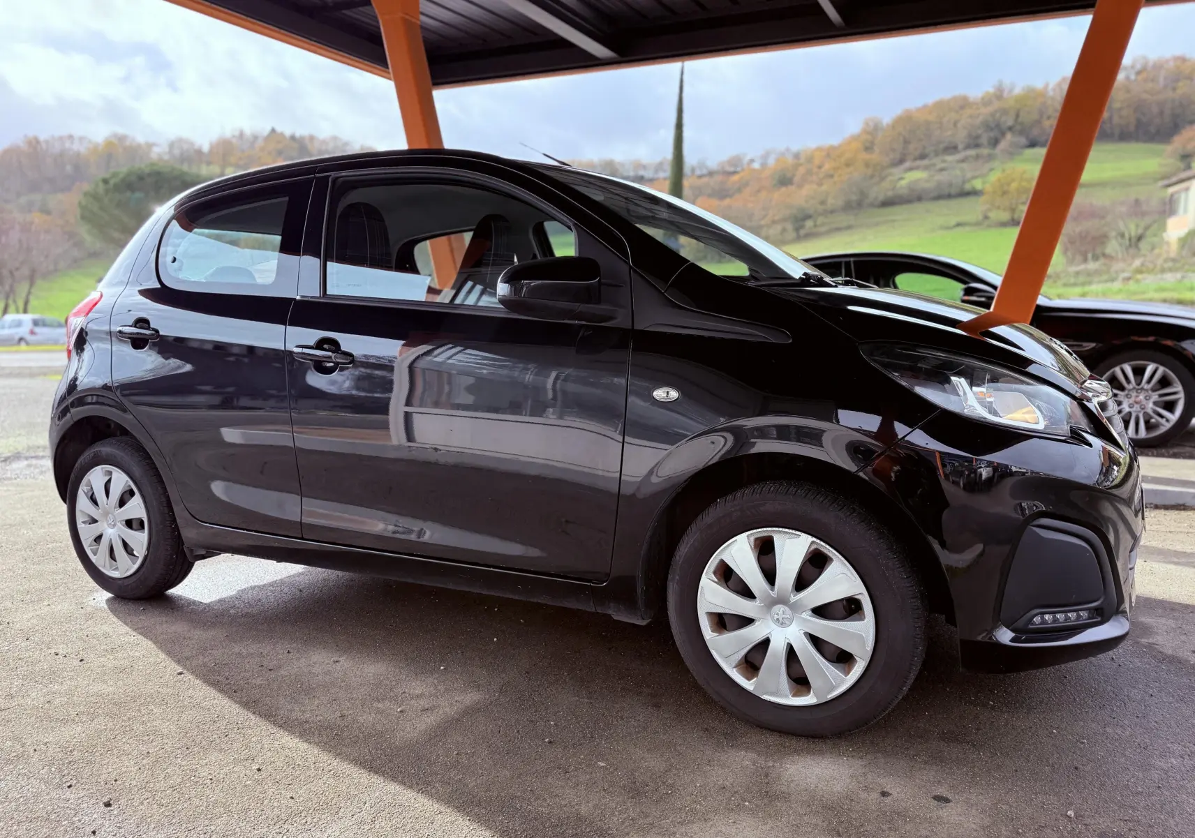 Peugeot 108 noire vue de profil côté gauche sous un abri avec jantes à enjoliveurs argentés.
