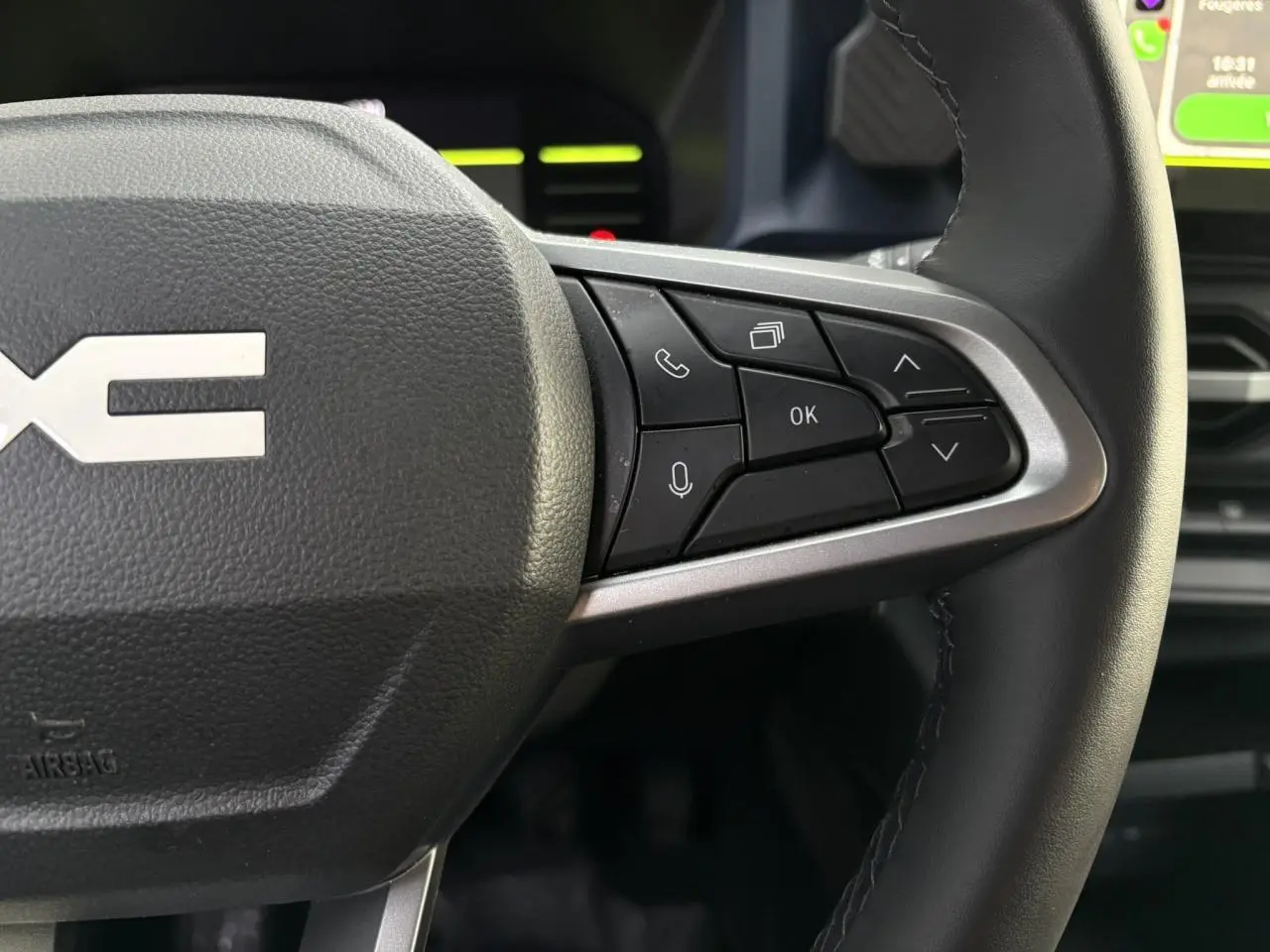 Gros plan sur les commandes au volant droit en cuir noir du Dacia Duster beige Sandstone 2024, avec écran tactile visible.