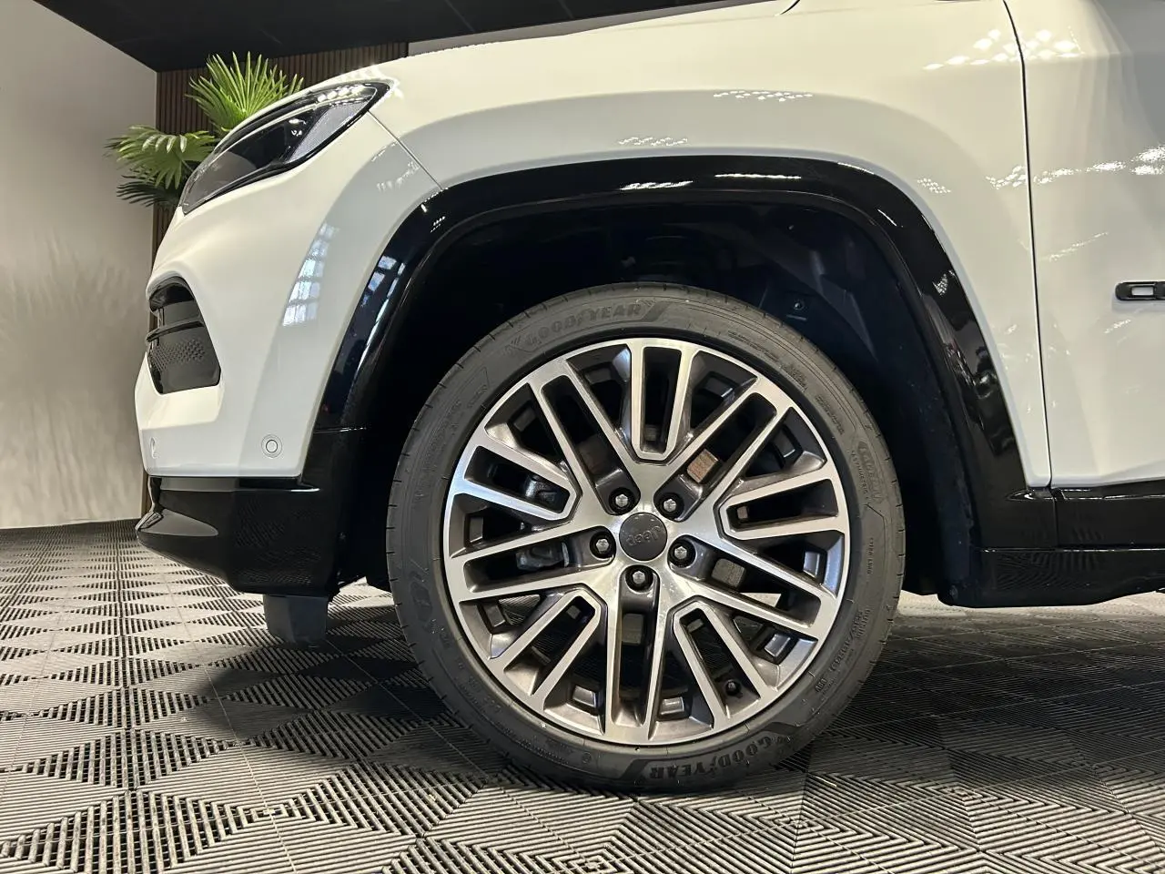 Gros plan sur la roue avant droite avec jante alliage 19'' du Jeep Compass blanc, soulignant l'aile et le pare-chocs noir.