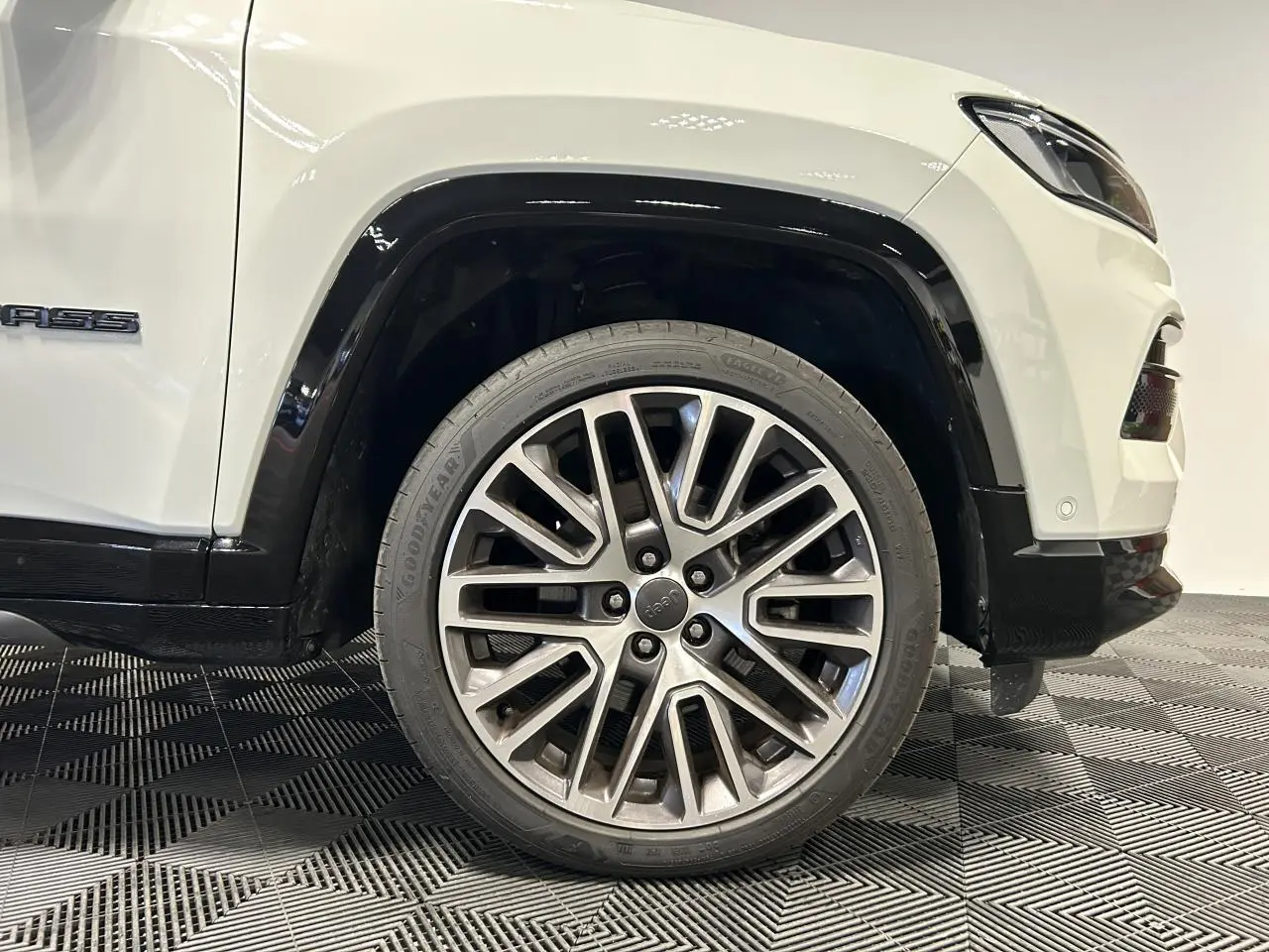 Gros plan sur la roue avant droite en jante alliage 19'' du Jeep Compass blanc avec entourage noir brillant.