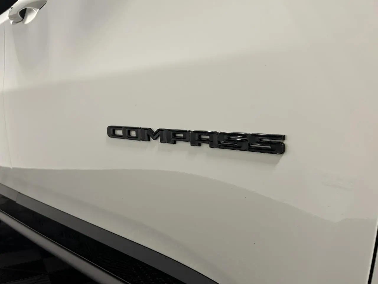Gros plan sur l’inscription Compass en noir sur la portière blanche d’un Jeep Compass 2024.