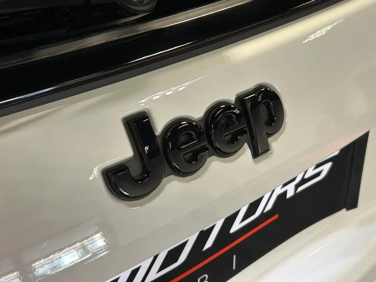Gros plan sur le logo Jeep noir brillant sur la carrosserie blanche Alpine White du Compass 2024.