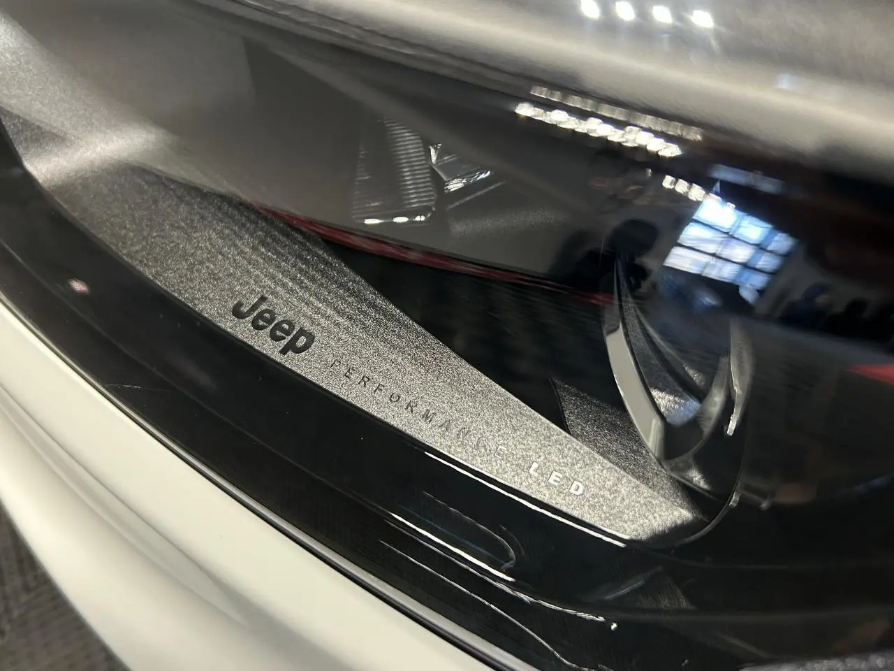 Gros plan sur le phare avant LED du Jeep Compass blanc avec inscription "Jeep Performance LED" visible.