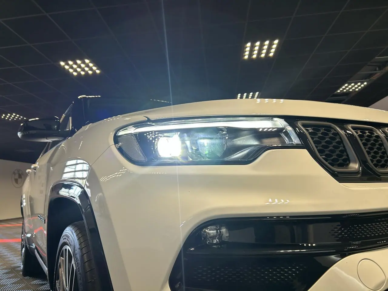 Vue 3/4 avant gauche d’un Jeep Compass blanc avec toit noir et phares LED allumés en intérieur showroom.