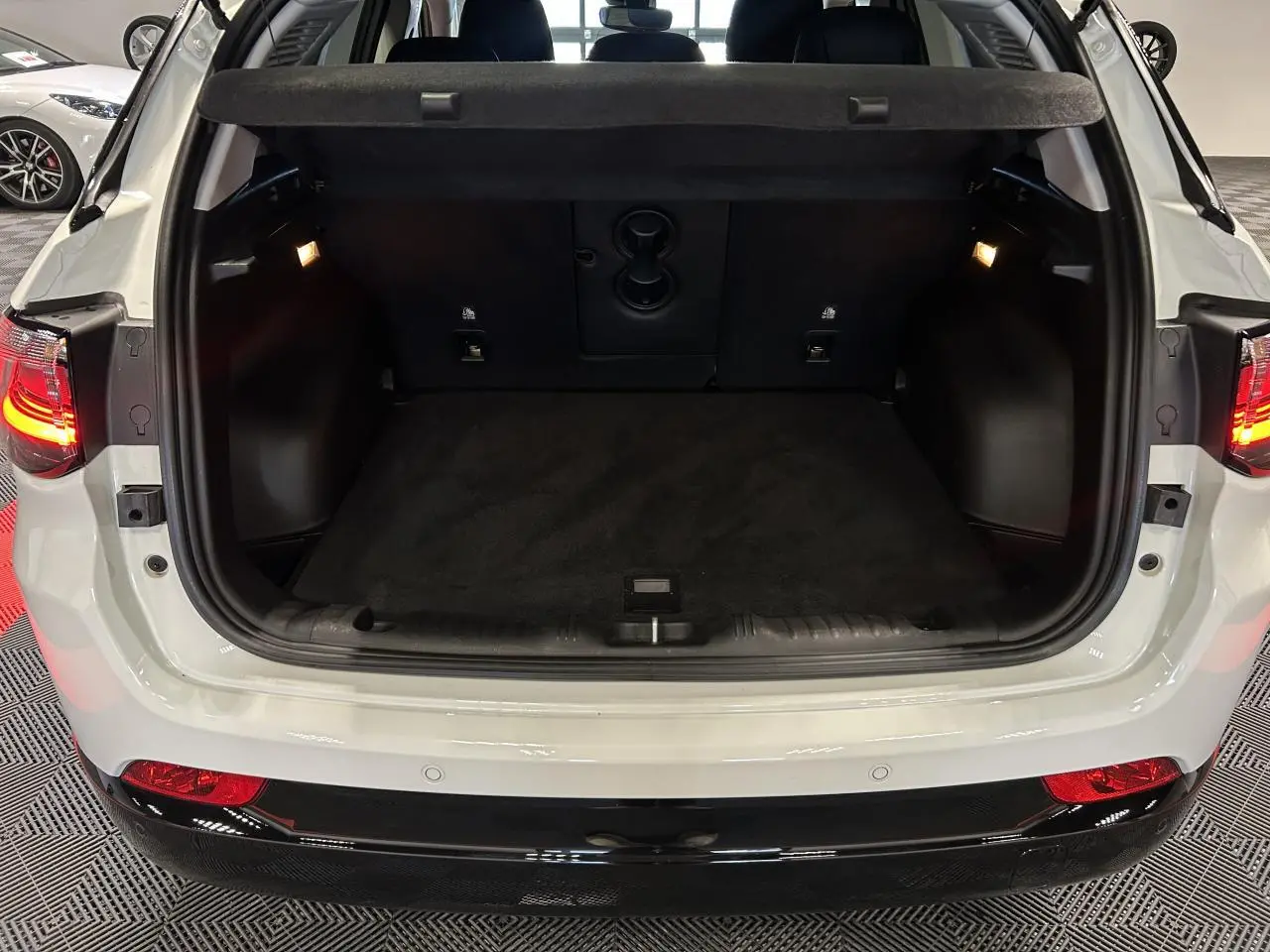 Coffre ouvert vu de l'arrière d'un Jeep Compass blanc avec intérieur noir et feux arrière allumés.