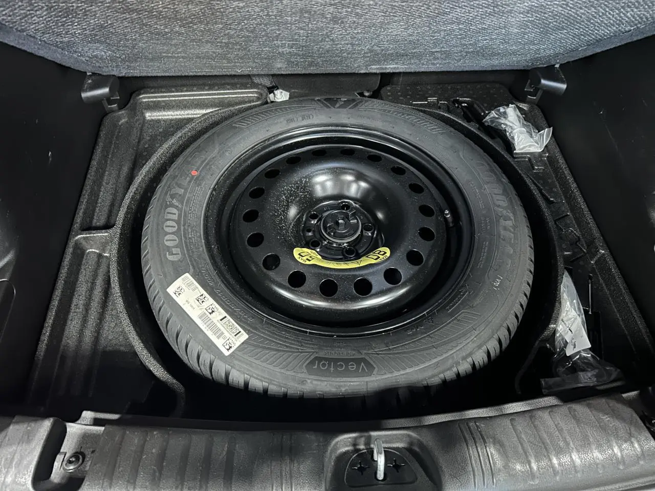 Roue de secours temporaire noire dans le coffre du Jeep Compass 2024 blanc, vue en plongée sur le pneu Goodyear.