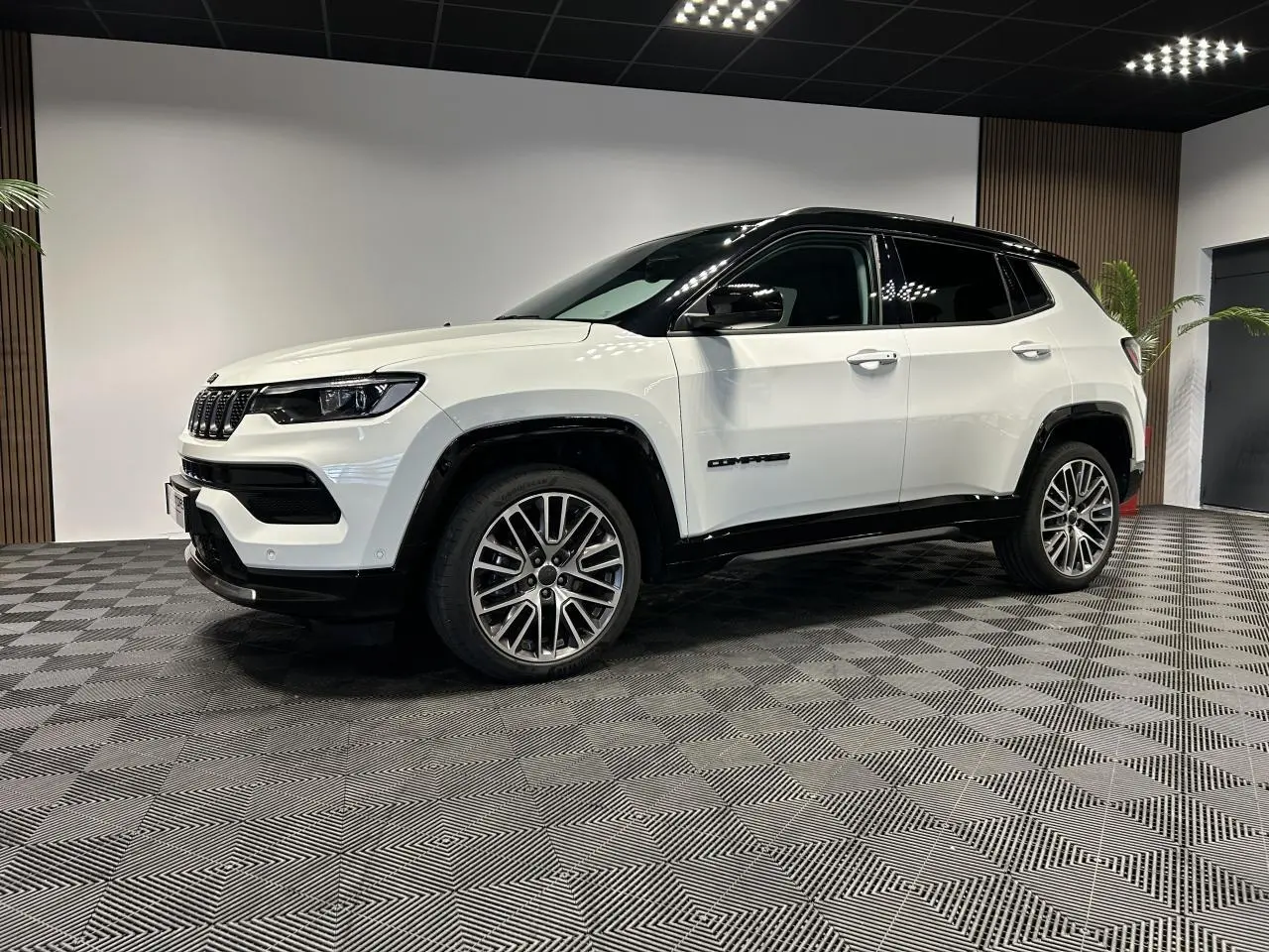 Jeep Compass blanc vue 3/4 avant droit avec toit noir et jantes alliage 19 pouces dans un showroom.