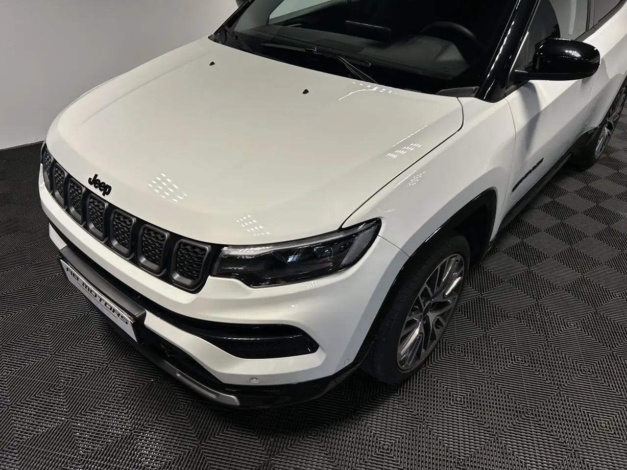 Vue 3/4 avant droit du Jeep Compass blanc avec toit noir et jantes alliage 19 pouces sur sol intérieur.