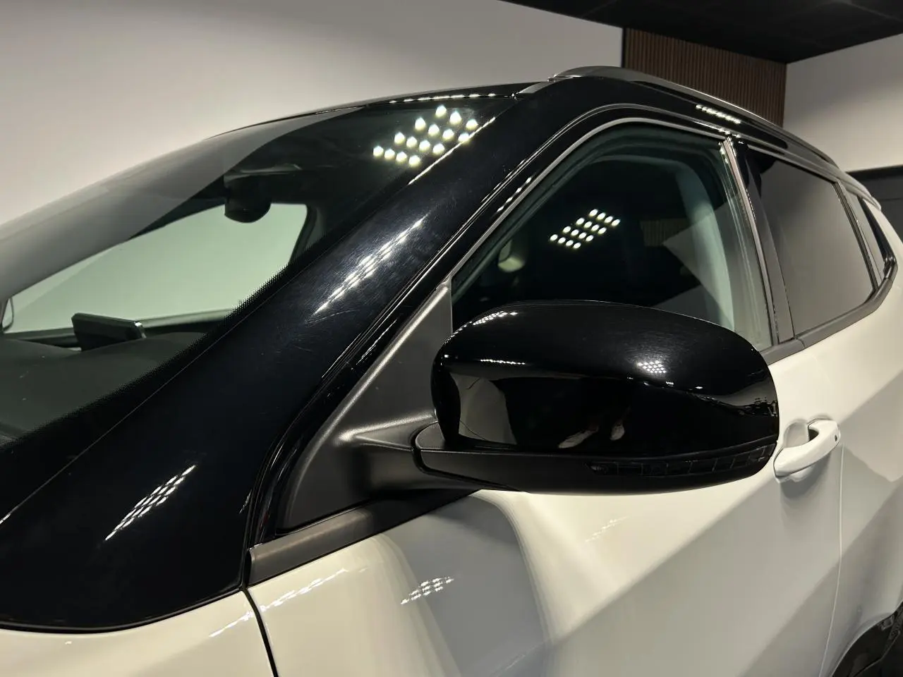 Gros plan sur le rétroviseur côté gauche noir brillant du Jeep Compass blanc avec toit noir, intérieur visible à travers la vitre.