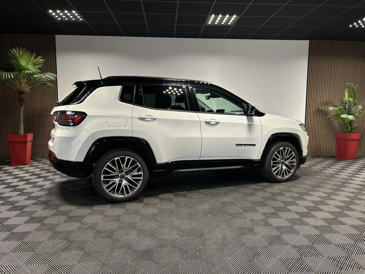 Jeep Compass blanc avec toit noir vu de profil côté gauche, jantes alliage 19 pouces et barres de toit noires.