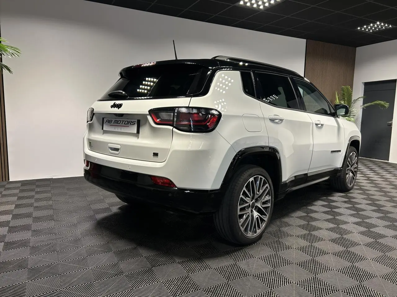 Jeep Compass blanc vue 3/4 arrière droit avec toit noir et jantes alliage 19 pouces en intérieur showroom.