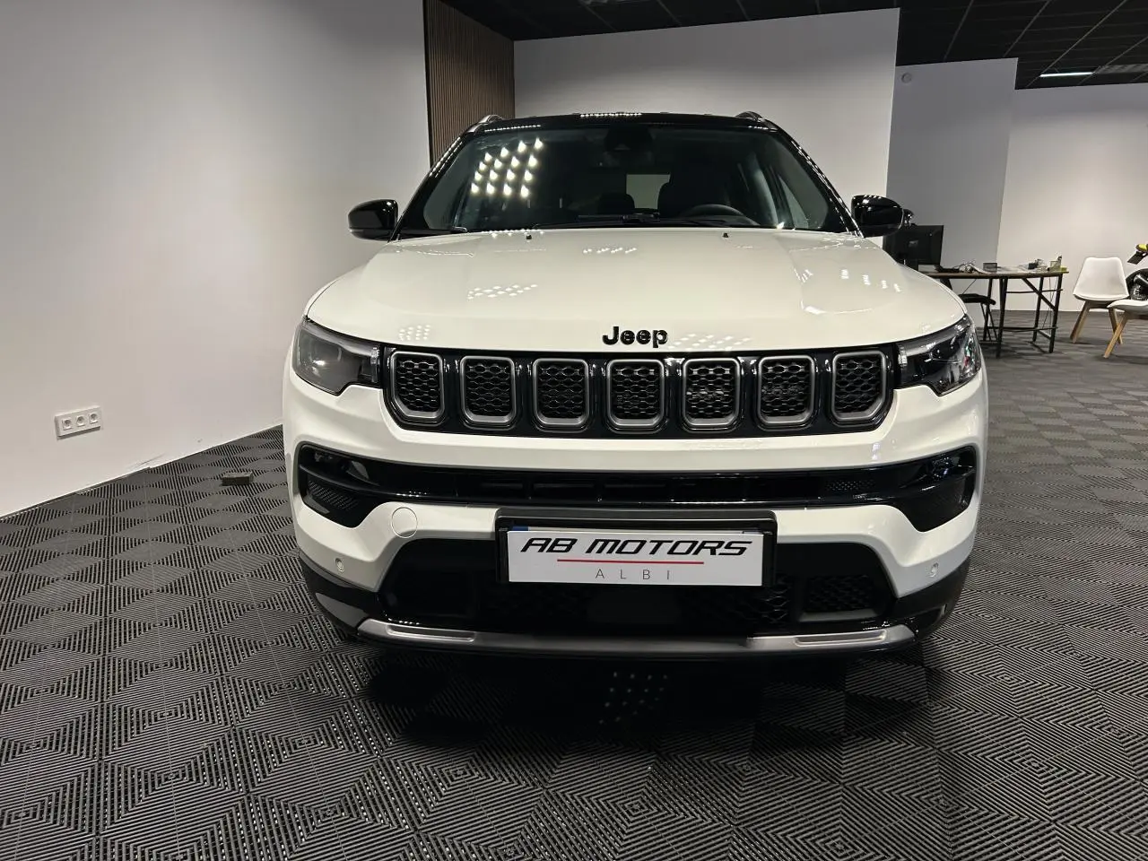 Vue frontale d'un Jeep Compass blanc avec calandre noire et toit noir dans un showroom intérieur.