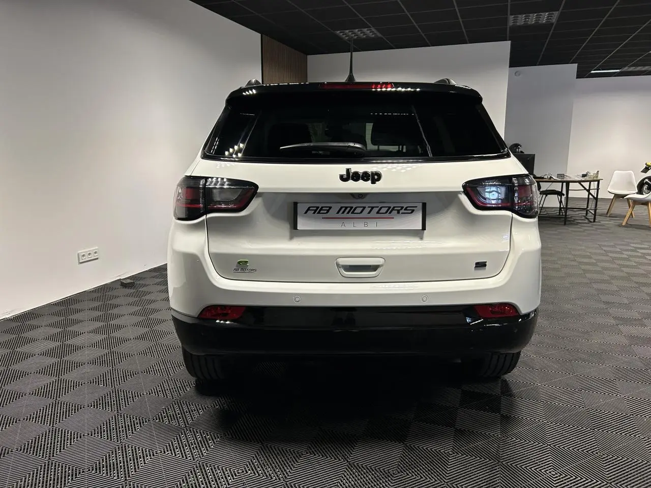 Vue arrière d'un Jeep Compass blanc avec toit noir, feux arrière LED et logo Jeep bien visible.