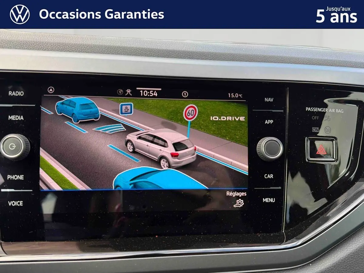Écran tactile central montrant l’assistance à la conduite avec véhicule gris en vue 3/4 arrière dans une Polo 2025 rouge.