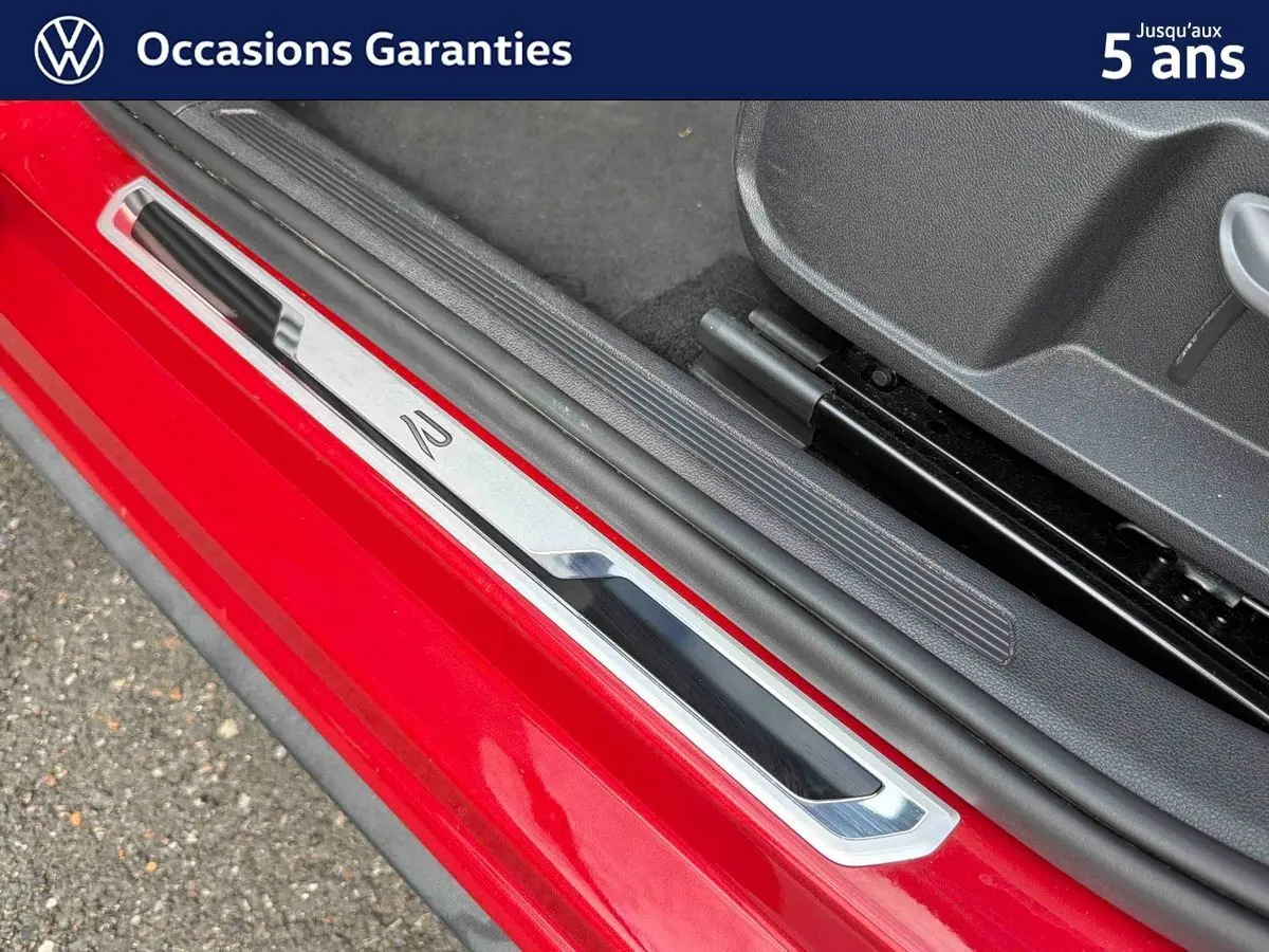 Gros plan sur la seuil de porte côté conducteur rouge métallisé de la Volkswagen Polo 2025 avec insert chromé et logo R.