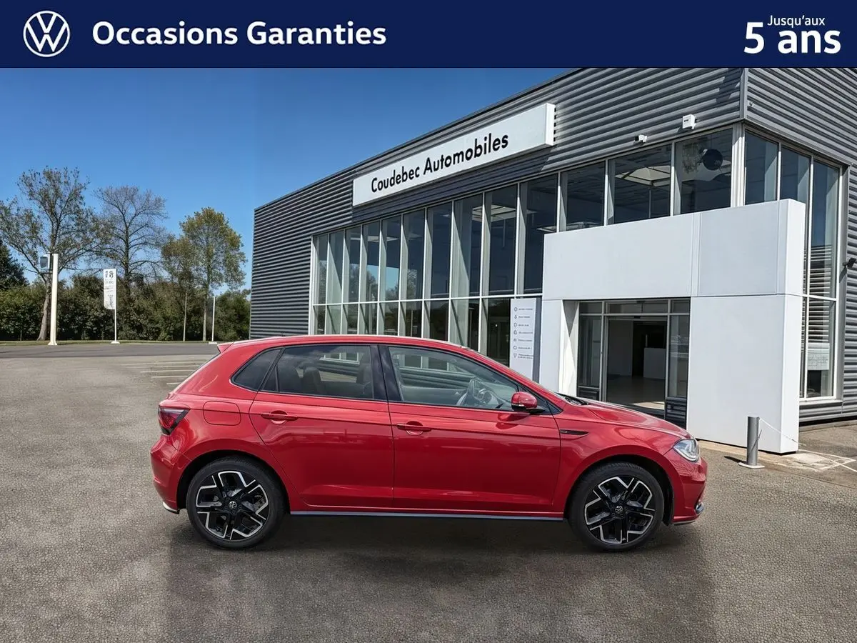 Volkswagen Polo rouge vue de profil côté gauche, garée devant un bâtiment moderne de concession.