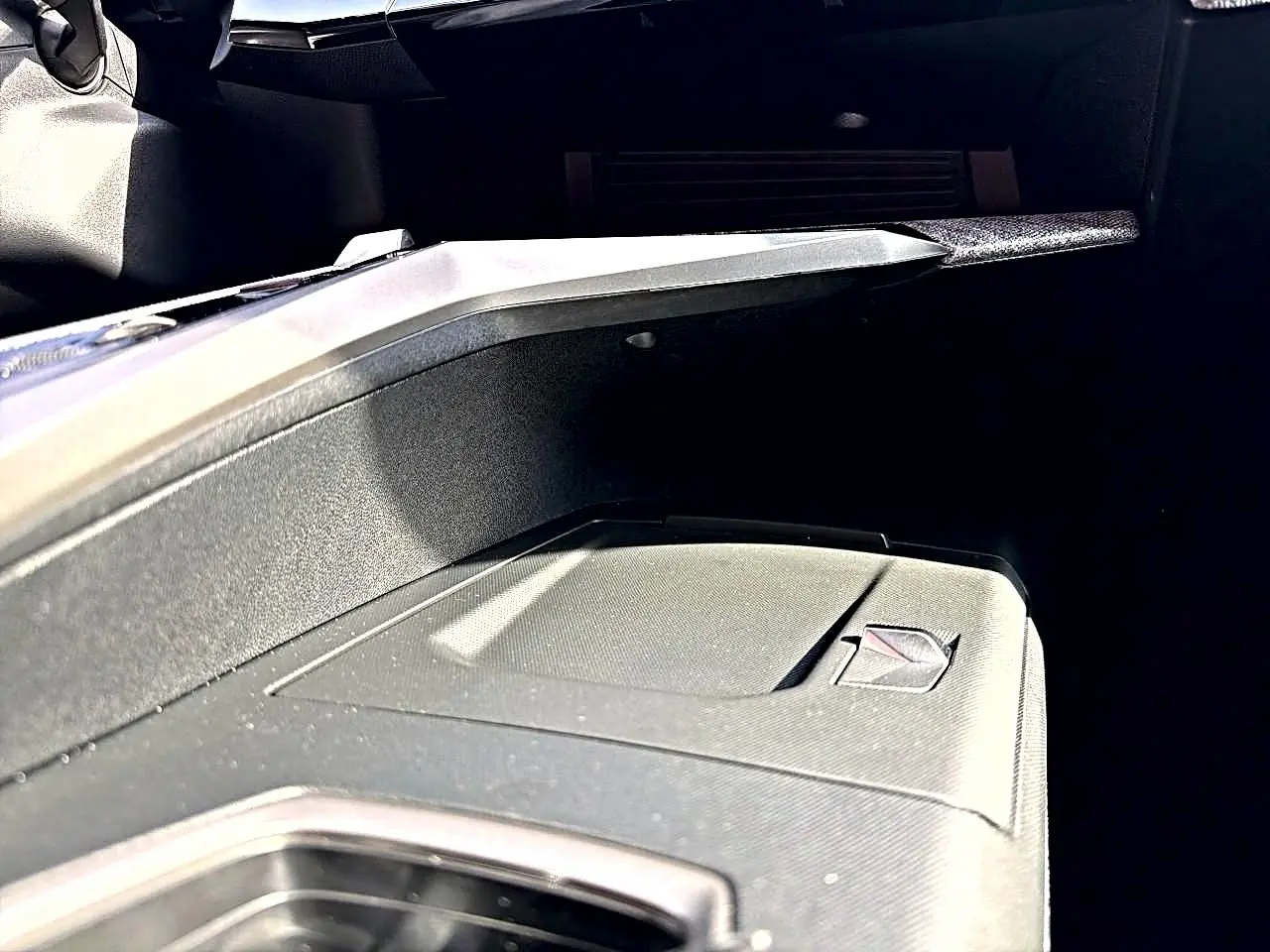 Gros plan sur la boîte à gants fermée noire du Peugeot 5008 Hybrid 145 GT e-dcs6, intérieur sombre.
