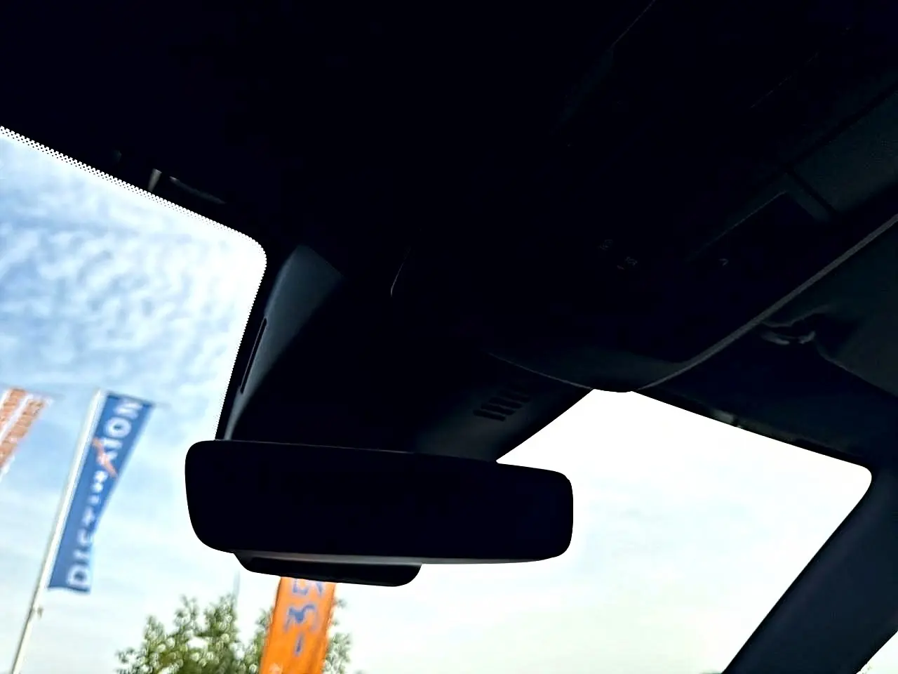 Vue intérieure du rétroviseur central d'un Peugeot 5008 noir, avec ciel et drapeaux visibles à l'extérieur.