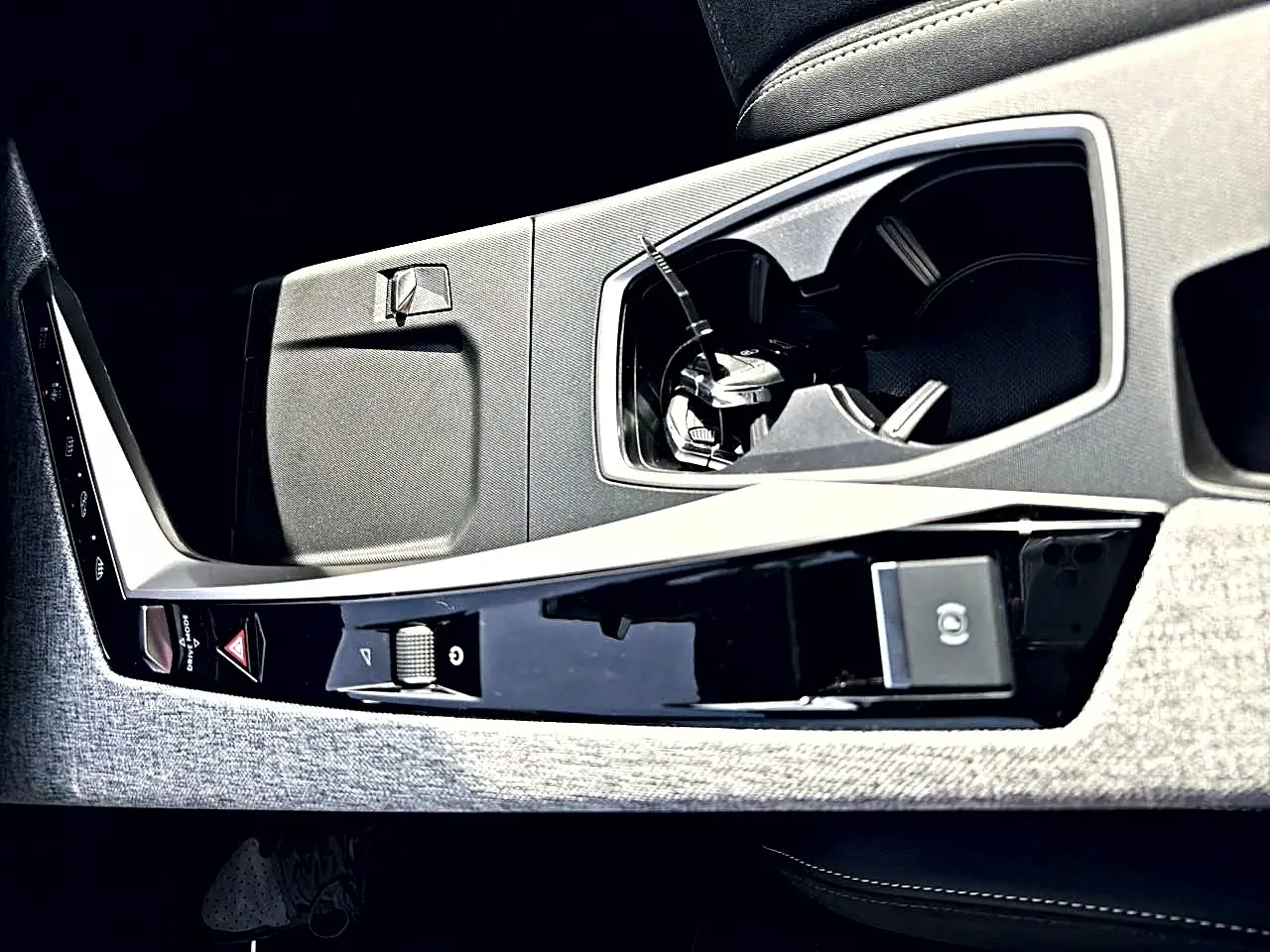 Gros plan de la console centrale intérieure du Peugeot 5008 Hybrid noir, avec porte-gobelets et commandes électroniques.