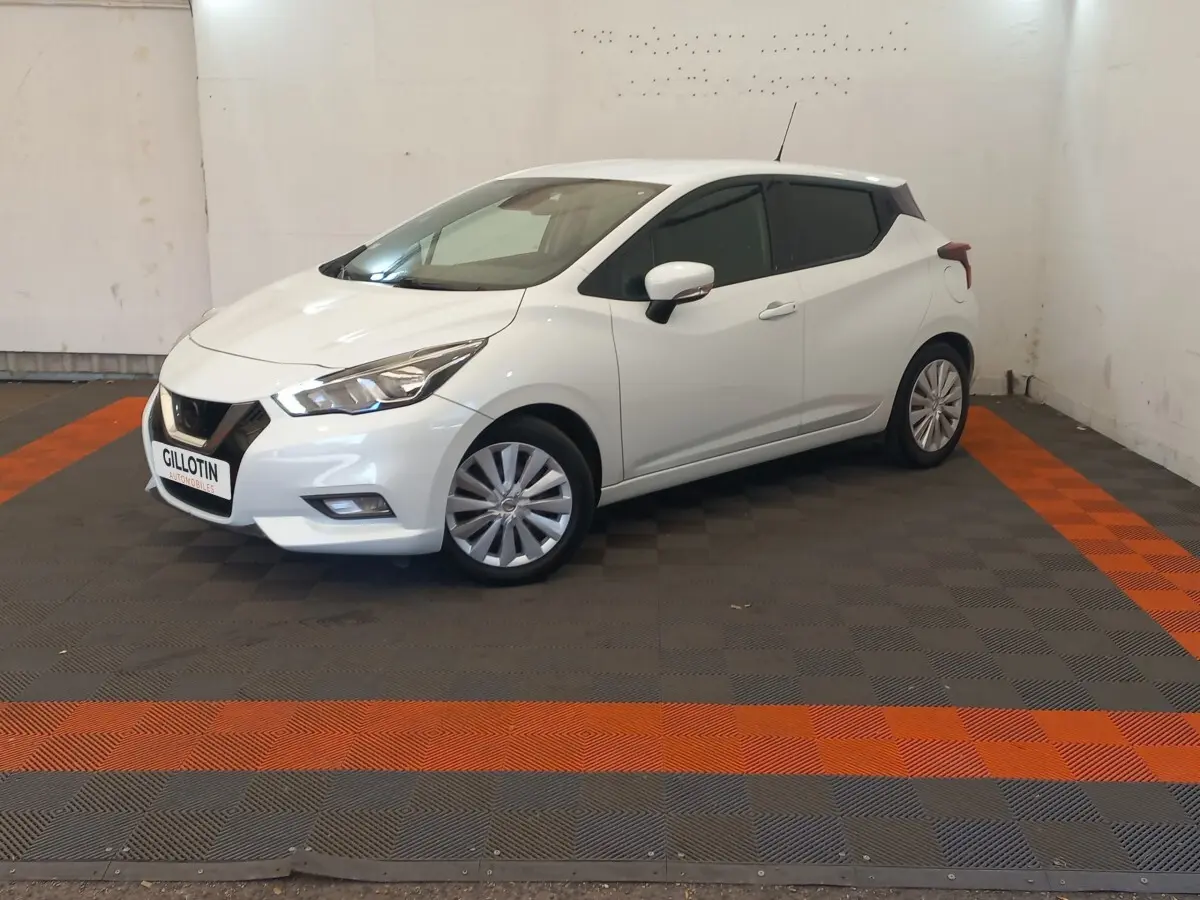 Nissan Micra blanche vue 3/4 avant droit, avec jantes alliage et feux avant distinctifs en intérieur neutre.
