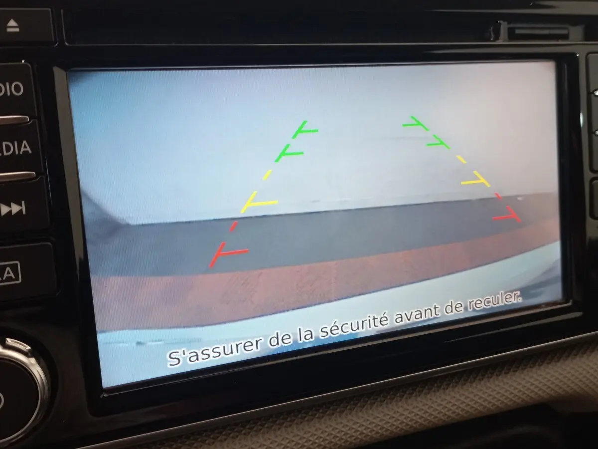Écran tactile de la Nissan Micra blanc montrant la caméra de recul avec guidage coloré et message de sécurité.