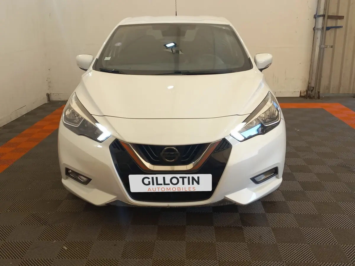 Vue frontale d'une Nissan Micra blanche avec phares LED allumés et calandre noire brillante.
