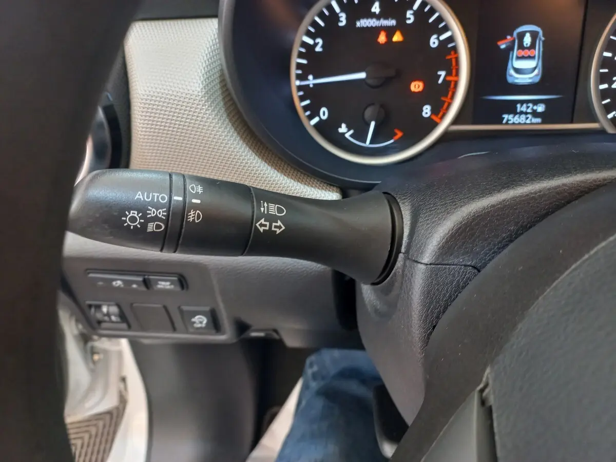 Gros plan sur le commodo gauche du volant noir d'une Nissan Micra blanche, avec tableau de bord et compte-tours en arrière-plan.