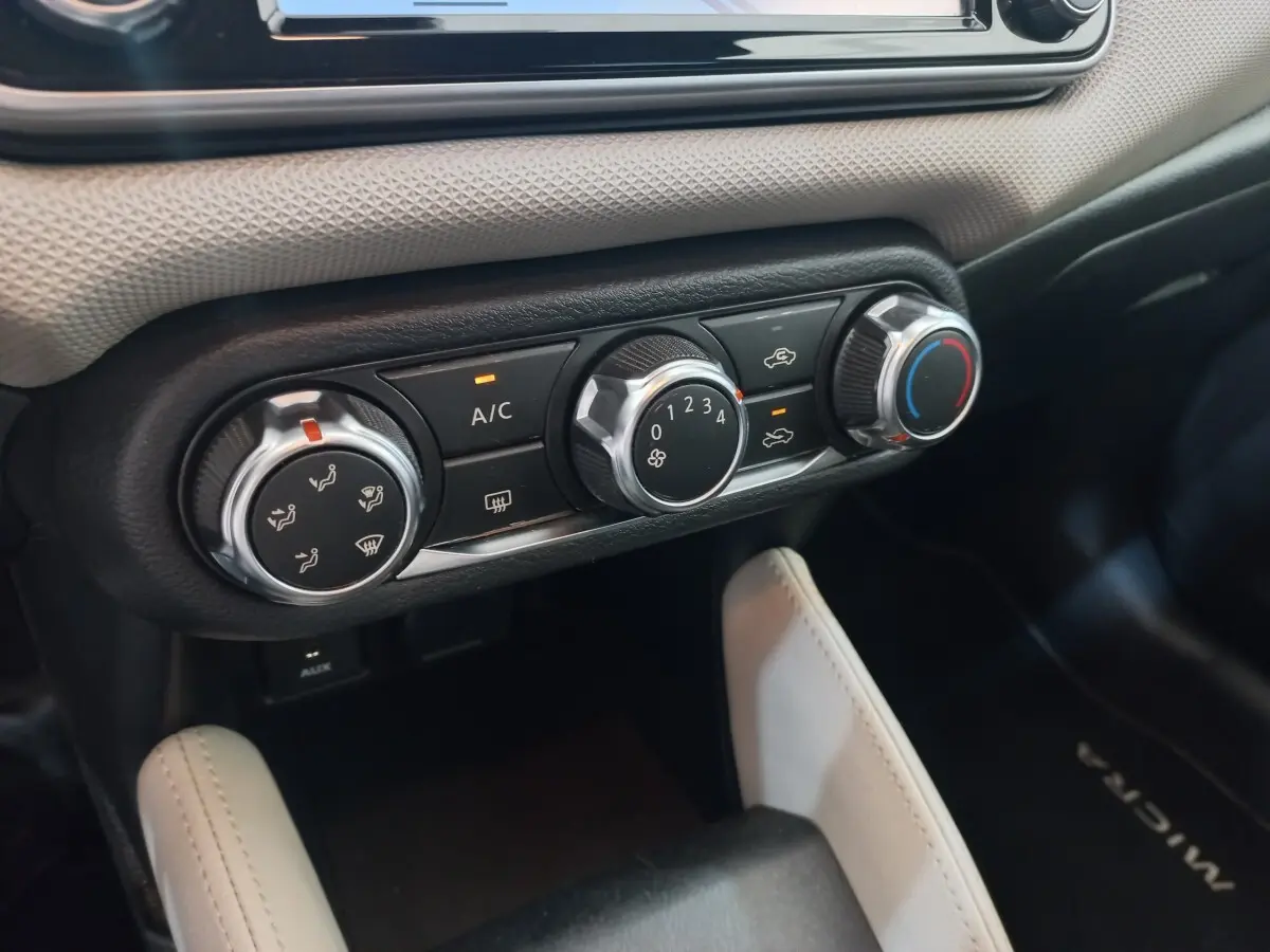 Gros plan sur les commandes de climatisation noires et argentées du tableau de bord d’une Nissan Micra blanche.