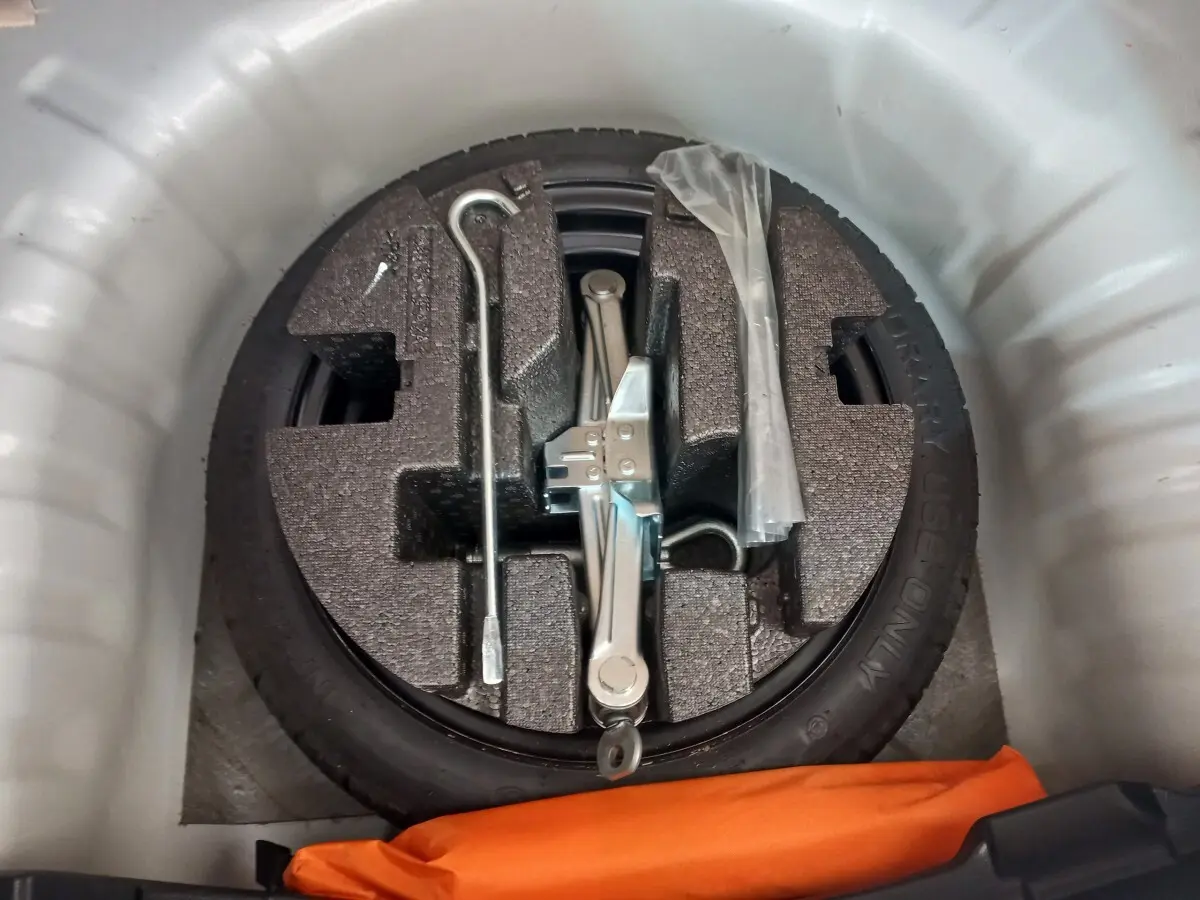 Roue de secours galette noire avec cric et outils dans le coffre blanc d’une Nissan Micra IG-T 90 Business Edition.