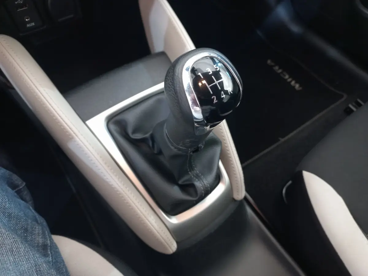 Gros plan sur le levier de vitesse manuel noir entouré de garnitures beiges dans l’habitacle d’une Nissan Micra blanche.