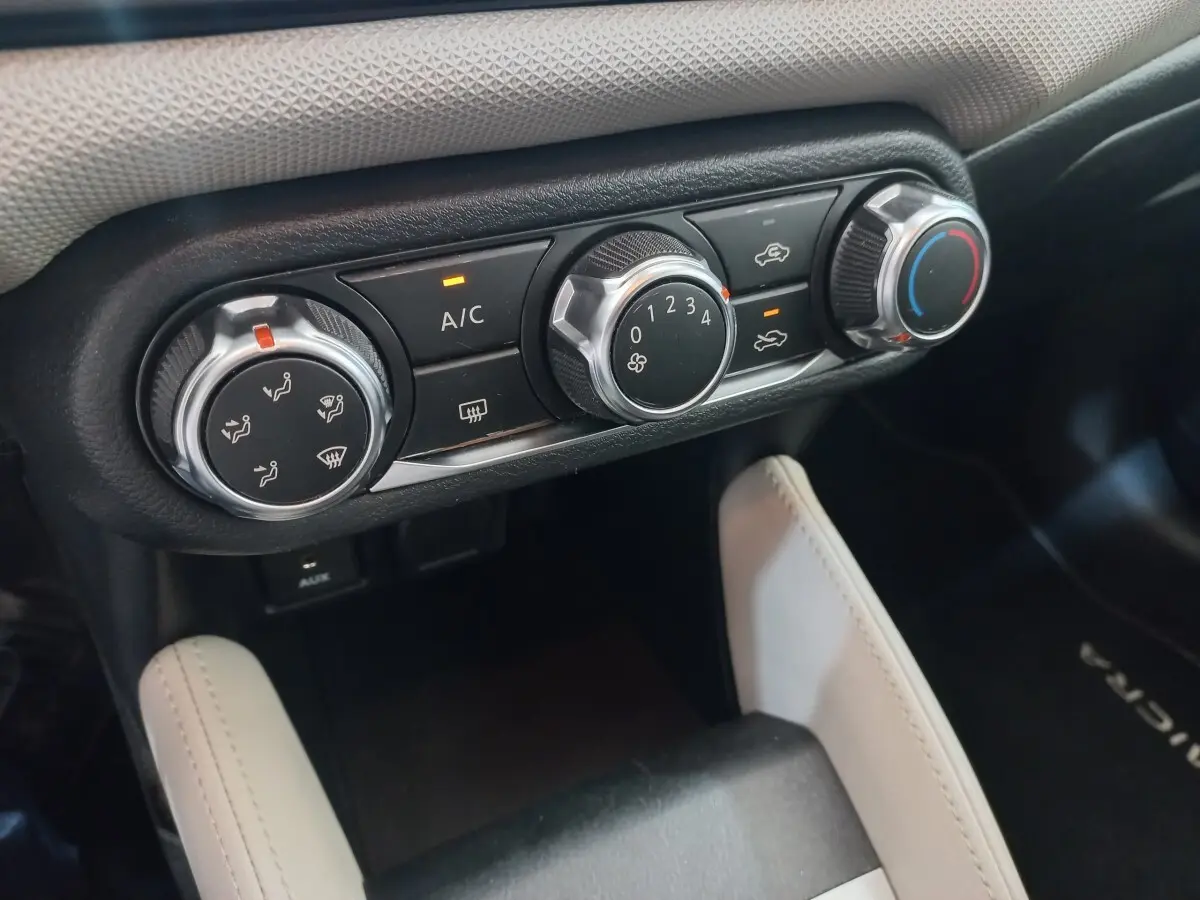 Gros plan sur les commandes de climatisation noires et argentées dans l'habitacle d'une Nissan Micra blanche.