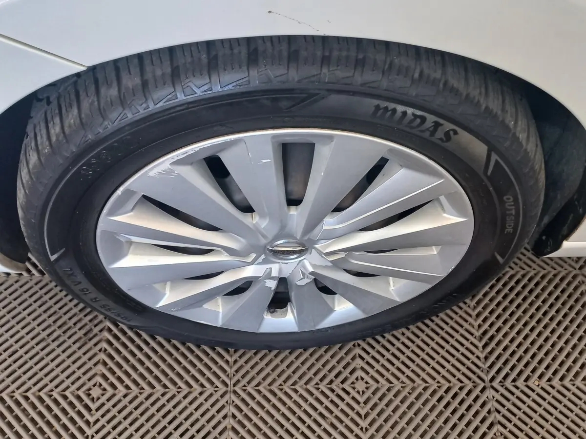 Gros plan sur la roue avant droite d’une Nissan Micra blanche, jante en alliage avec logo Nissan au centre.