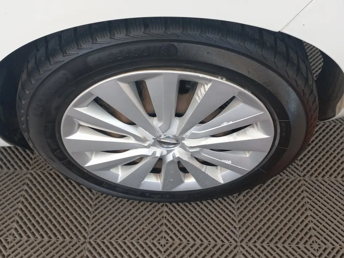 Gros plan sur la roue avant gauche d'une Nissan Micra blanche, jante en alliage avec éclats de peinture visibles.