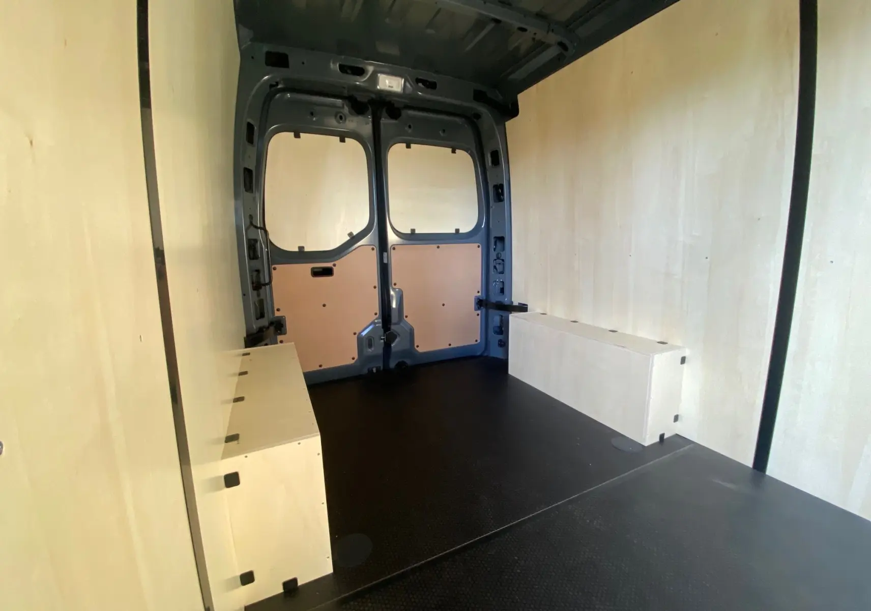 Vue intérieure arrière du Renault Master gris urbain 2025 avec aménagement bois et plancher noir antidérapant.