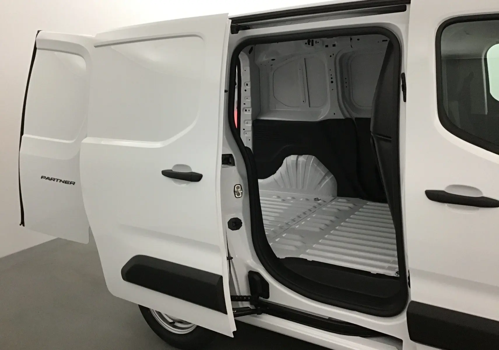 Vue latérale gauche d’un Peugeot Partner blanc 2025 avec porte coulissante ouverte montrant l’espace de chargement vide.