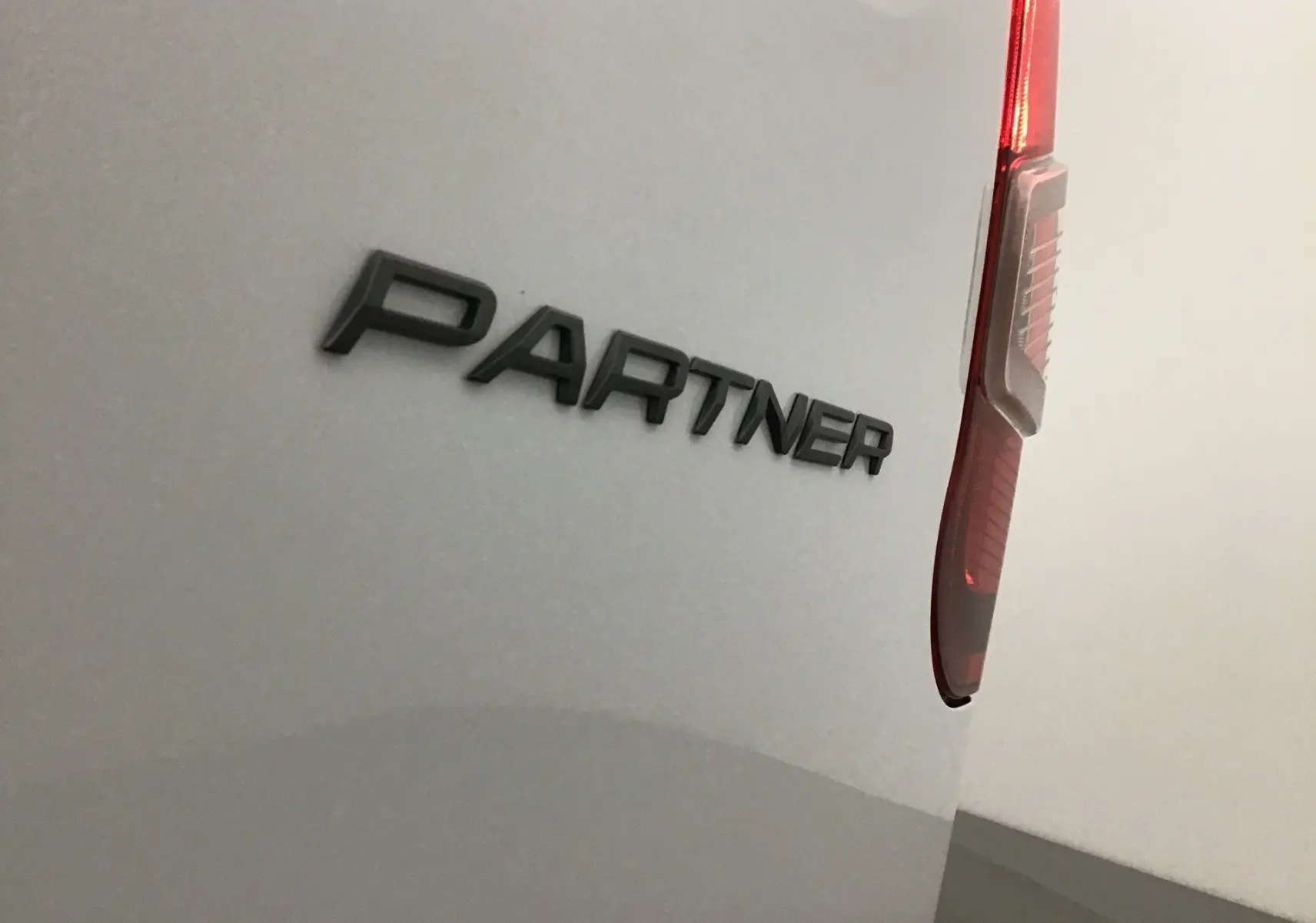 Gros plan sur l'arrière droit blanc du Peugeot Partner 2025 avec le logo "PARTNER" et le feu arrière visible.