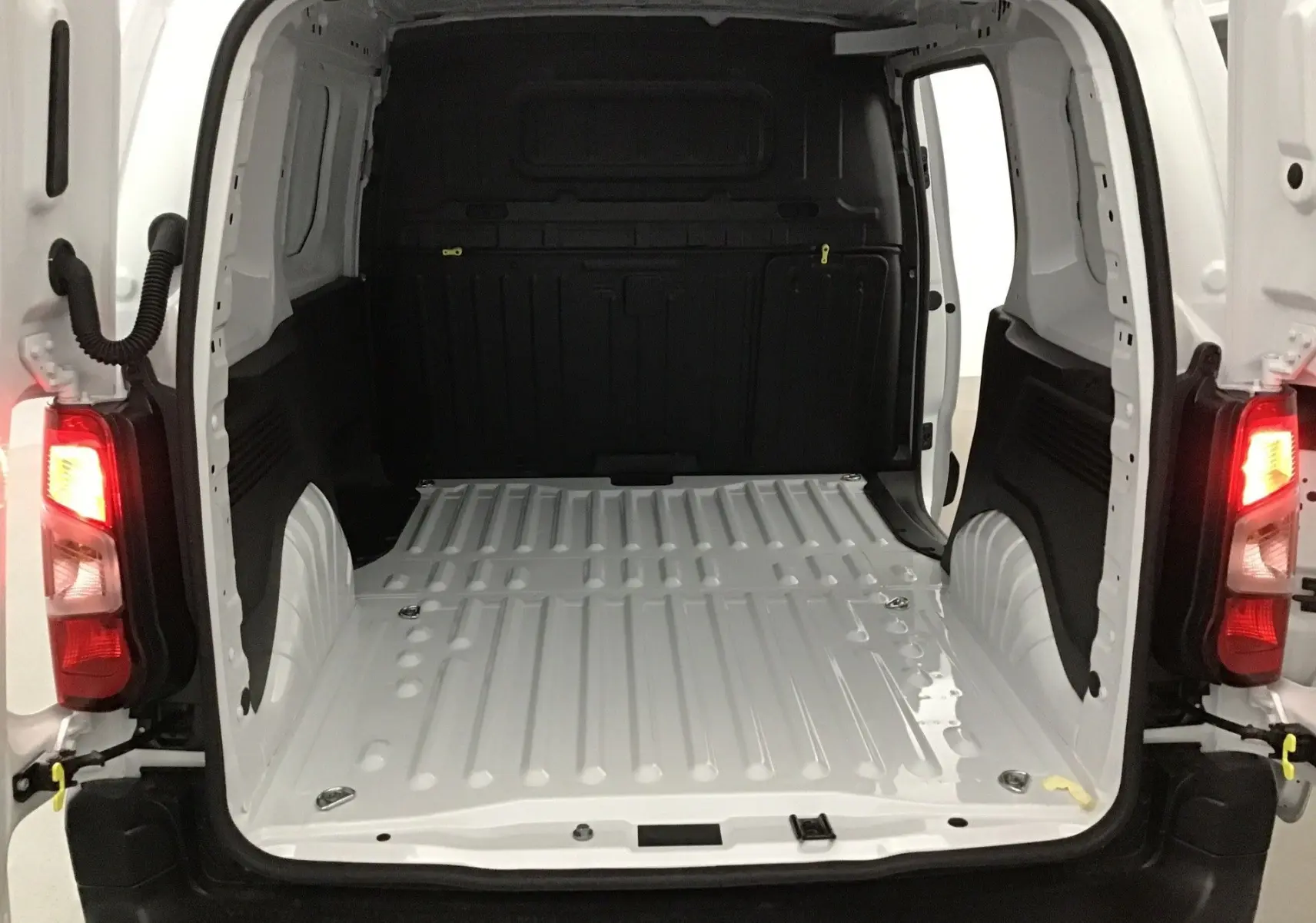 Vue arrière ouverte du Peugeot Partner blanc 2025, montrant l'espace de chargement vide et les feux arrière allumés.