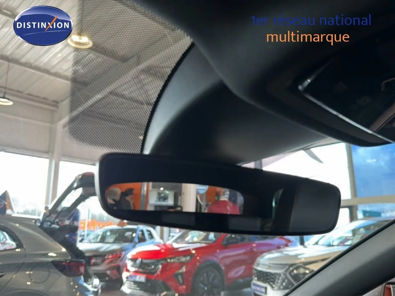 Rétroviseur intérieur montrant en reflet plusieurs véhicules en concession, dont un SUV rouge et une voiture grise.