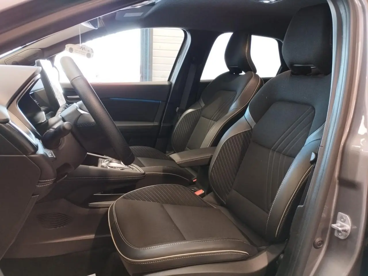 Vue intérieure côté gauche des sièges avant noirs avec surpiqûres blanches dans une Renault Symbioz gris cassiopée.