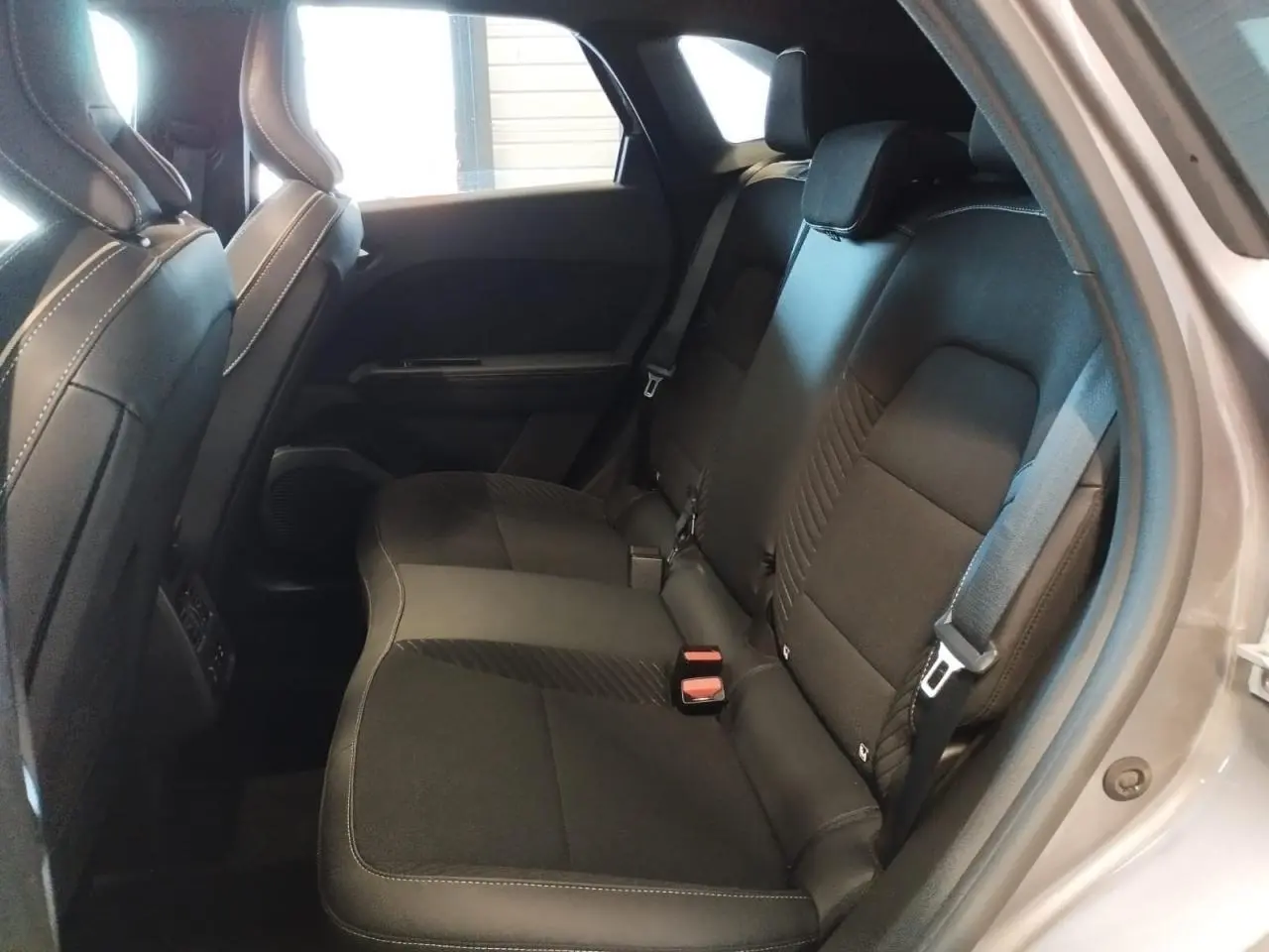 Vue intérieure arrière côté droit du Renault SYMBIOZ 2025, sièges tissu noir avec surpiqûres blanches, portière gris cassiope visible.