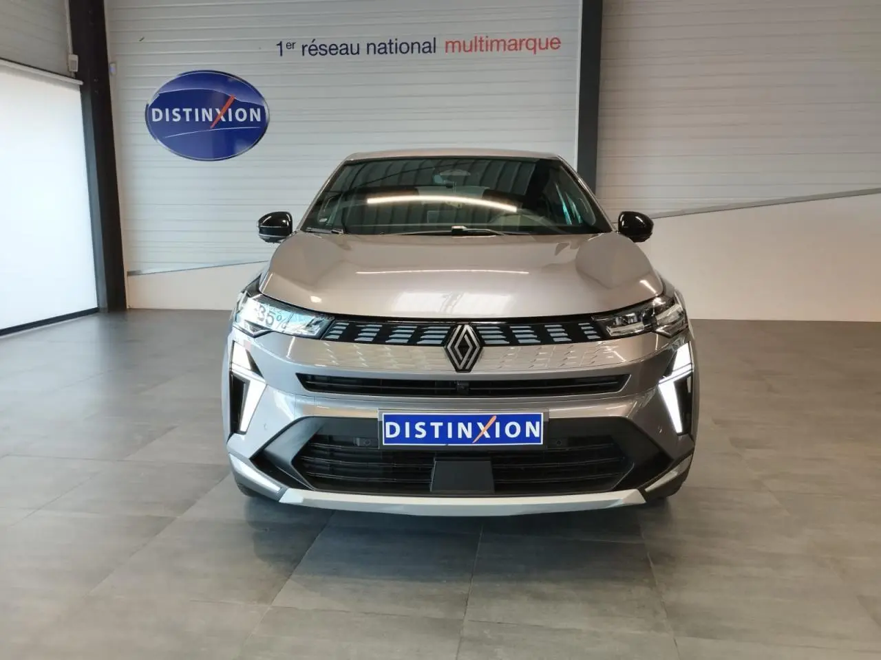 Vue de face du Renault Symbioz gris Cassiopée avec calandre 3D et feux LED verticaux allumés en intérieur showroom.