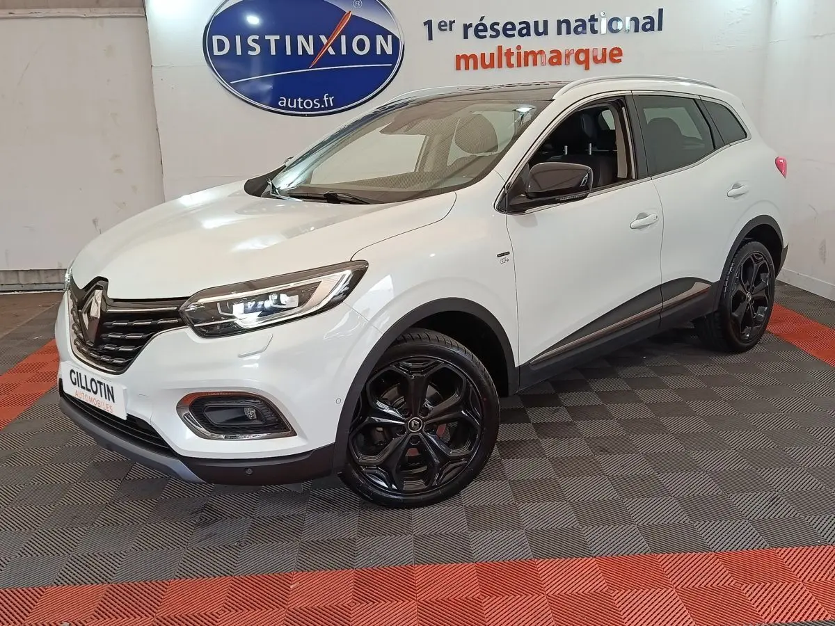 Renault Kadjar blanc vue 3/4 avant droit, jantes noires brillantes et phares LED allumés en intérieur showroom.